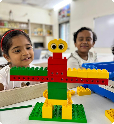 Two young children smiling beside a colourful robot they built from blocks