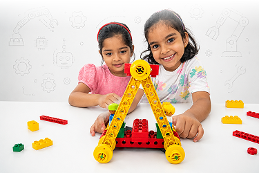 Two young girls smiling while building a yellow and red robot from construction blocks