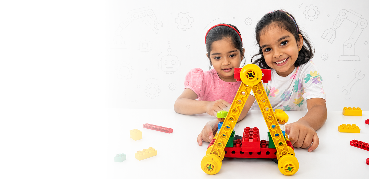 Two young girls smiling while building a yellow and red robot from construction blocks