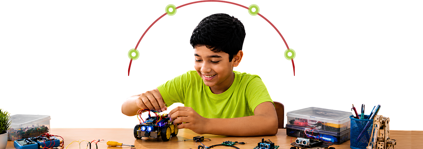 A smiling boy in a green T-shirt building a small robot car surrounded by electronics kits